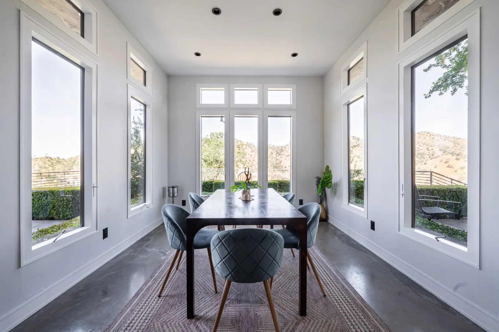 Glass-walled dining room with a long table and hill views